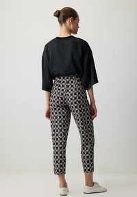 Black oversized shirt with wide sleeves paired with high-waisted patterned trousers in black and cream, complemented by white shoes.