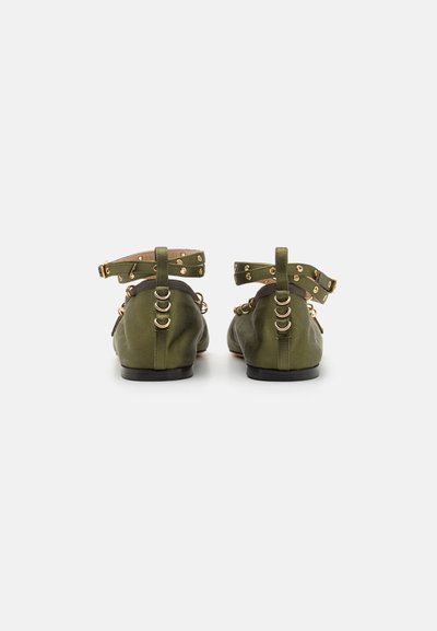 Green fabric flats with gold accents, ankle straps, and decorative hardware. Low heel with a smooth texture, featuring a rounded toe design.