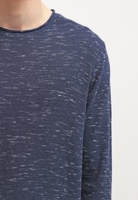 Pull bleu marine en maille texturée avec col ras du cou et manches longues, présentant un motif moucheté.