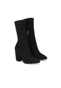 Botas de tobillo de ante negro con punta afilada y cierre de cremallera en el lateral. El tacón es grueso y tiene un acabado mate.