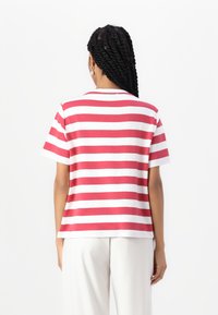 Camiseta a rayas rojas y blancas con mangas cortas y escote redondo. Presenta un corte holgado, una textura de tejido suave y un dobladillo recto.
