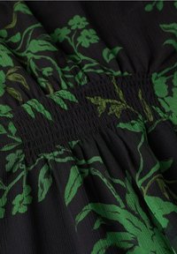 Tissu noir avec un motif floral vert ; présente un détail de smocks froncés à la taille, créant un contraste visuel texturé.