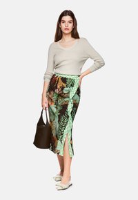 Hellgrauer, gestrickter Pullover mit Rundhalsausschnitt; dunkelblumenbedruckter Rock mit grünen Karomusterakzenten und seitlichem Schlitz; schwarze Handtasche; grüne Ballerinas mit Schleife.