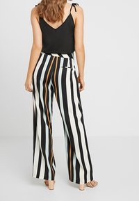 Haut sans manches noir et pantalon large à rayures verticales noires, blanches et pastel ; tissu lisse avec une coupe décontractée et des poches latérales.