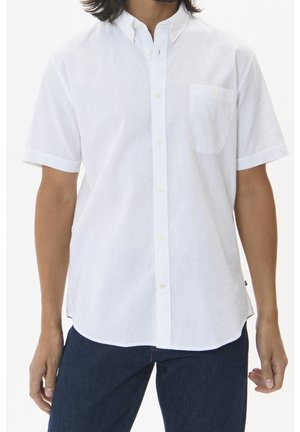 Buste masculin portant une chemise blanche à manches courtes avec poche poitrine et jean bleu foncé sur fond blanc.