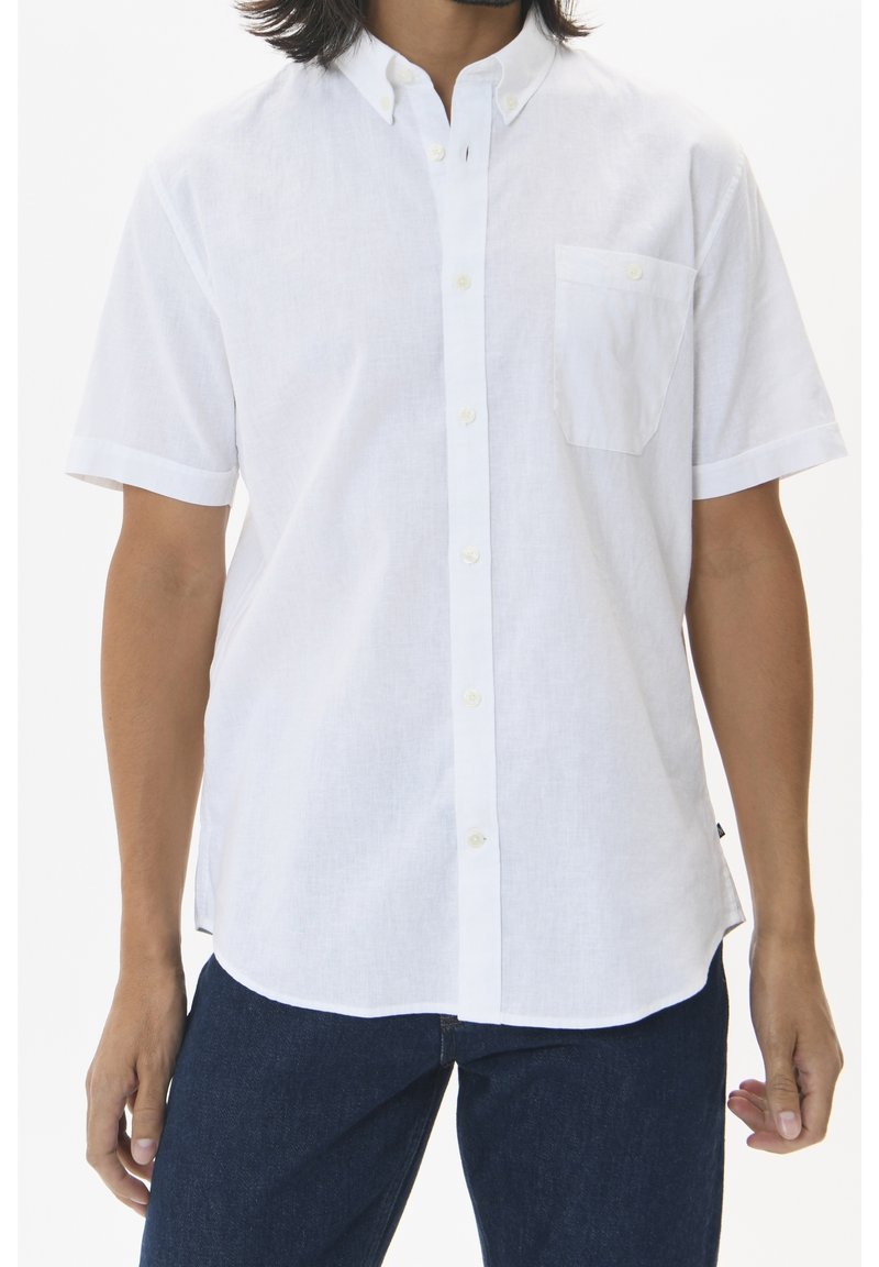 Buste masculin portant une chemise blanche à manches courtes avec poche poitrine et jean bleu foncé sur fond blanc.