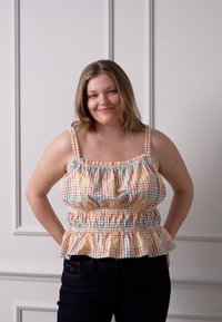 Top peplum xadrez em cores pastel, com alças ajustáveis e detalhes franzidos. O tecido é leve e tem uma textura suave.