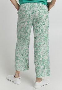 Pantalones sueltos con estampado floral en verde y blanco, con una cinturilla elástica y bolsillo laterales, combinados con zapatillas blancas.