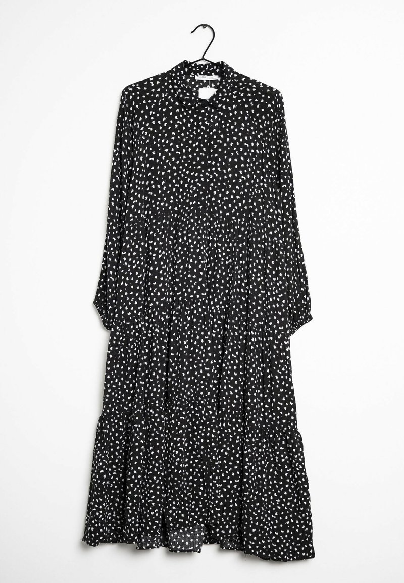 Robe midi noire à manches longues avec motif de points blancs irréguliers, volants froncés et col, suspendue sur un cintre noir sur fond blanc.