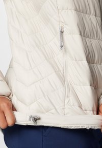 Giacca imbottita color crema con motivo a zigzag, dotata di una cerniera e un cordoncino all'orlo per la regolabilità.