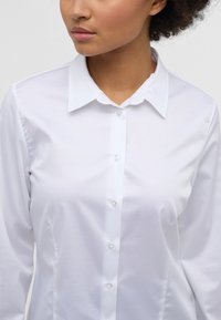 White long-sleeve shirt with a classic collar, featuring a button-down front and smooth, textured fabric. Simple and clean design.