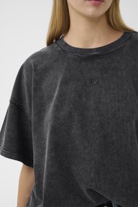 Oversized svart bomull t-skjorte med rund hals, korte ermer og subtil logo detalj på brystet; myk, teksturert stoff.