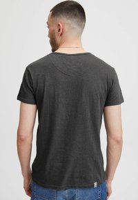 Czarnoszary t-shirt z krótkim rękawem i okrągłym dekoltem, o gładkiej fakturze i małej metce z logo na końcu.