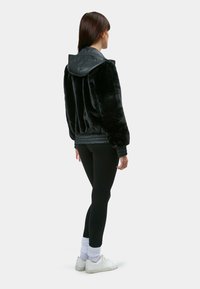 Sort faux fur jakke med en læderhætte, ribbede manchetter og kant. Sammen med sorte leggings og hvide sneakers med ribbede hvide sokker.