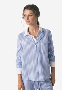 Lichtblauw gestreepte pyjama shirt met witte accenten, voorzien van een notch kraag, een voorzak en knoopsluiting. Lichtgewicht stoffen, ontspannen pasvorm.