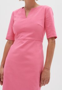 Tajtat rosa klänning med korta ärmar, V-ringning och slätt tyg; har en sömdetalj vid midjan och sidobystinsnitt.