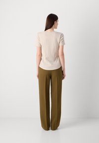 Tricou bej cu mânecă scurtă și tiv rotund, asortat cu pantaloni largi de culoare verde măsliniu, cu croială dreaptă și pliuri.