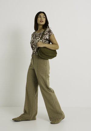 Haut à motifs marron, pantalon beige à jambes larges, sac à main vert olive et ballerines à motifs. Modèle se tenant contre un fond blanc.