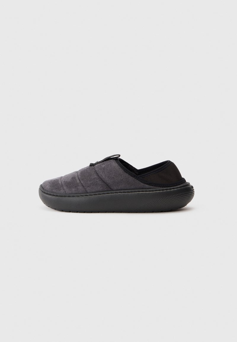 Sötétszürke, slip-on stílusú papucs, melynek steppelt szövet felsőrésze és vastag fekete gumi talpa van, a kényelem és az egyszerű viselet érdekében.