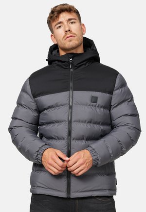 Chaqueta acolchada con cierre de cremallera. Color principal gris con sección superior negra. Cuenta con capucha y puños elásticos. Textura suave, diseño acolchado.