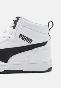 Baskets montantes en cuir synthétique blanc avec des accents noirs. Comporte un col rembourré, un logo en forme de swoosh noir et un revêtement texturé, avec des lacets plats.