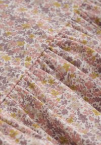 Blumenerstoff mit kleinen rosa, lila und gelben Blumen auf einem weißen Hintergrund, mit geraffter Textur und weichem Baumwollmaterial.