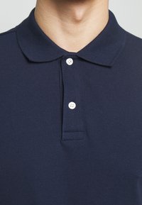 Navy blue polo shirt made of textured fabric, featuring a collar, three button placket, and short sleeves.
