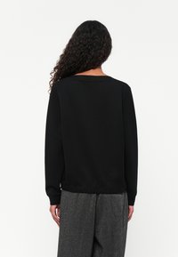 Zwarte sweatshirt met een relaxte pasvorm, ronde halslijn en lange mouwen. Het materiaal lijkt zacht met een gladde textuur. Eenvoudig ontwerp, geen extra details.