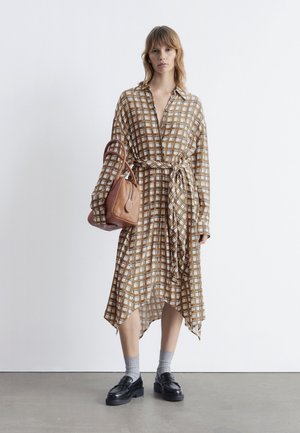 Brown and white checkered dress with long sleeves, a V-neck, belted waist, and asymmetrical hem; paired with a brown handbag and black shoes.