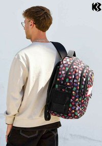 Sac à dos multicolore à forme incurvée, en tissu, avec des motifs de personnages de dessin animé sur fond noir, comprend une poche en mesh sur le côté.