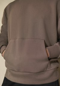 Brun sweatshirt med en blød tekstur, der har en frontlomme og elastiske manchetter, designet til komfort og afslappet brug.