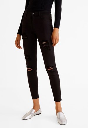 Zwarte skinny jeans met gescheurde knieën en een vijf-pocket ontwerp. Gstyle met een strakke zwarte top en metallic zilveren instappers.
