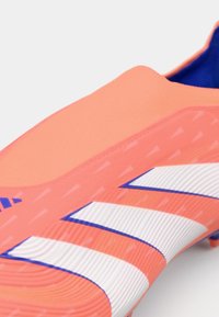 Bota de fútbol ligera con una parte superior sintética rosa, acentos de rayas blancas y azules, y una superficie texturizada para tracción y control.