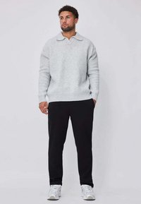 Pull gris clair en tricot avec col, poignets et ourlet côtelés, associé à un pantalon noir et des baskets blanches sur un fond uni.