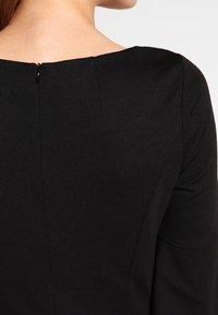 Czarna, dopasowana sukienka z gładką teksturą, okrągłym dekoltem i zapięciem na zamek błyskawiczny z tyłu. Prosty fason z minimalnym zdobieniem.