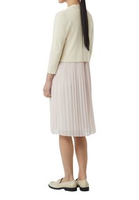 Lichtbeige, korte mouwen jack gecombineerd met een geplooide roze jurk. De jurk is kniehoog met een textuurafwerking, aangevuld met crèmekleurige loafers.