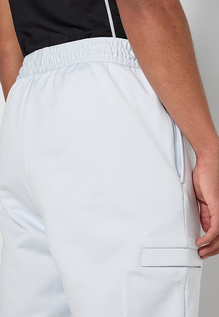 Close-up van een persoon in lichtblauwe mesh shorts met elastische tailleband en zijzakken, hand rustend nabij de opening van de zak.