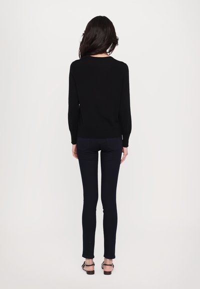 Pulover negru tricotat, cu mâneci lungi și decolteu rotund, asociat cu blugi strâmți de culoare albastru închis. Design simplu, fără modele sau elemente de hardwear.