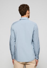 Helleblaue Langarmbluse mit Button-Down-Kragen und abgerundetem Saum. Aus glattem Stoff gefertigt, mit Knopfmanschetten und schlichtem Design.