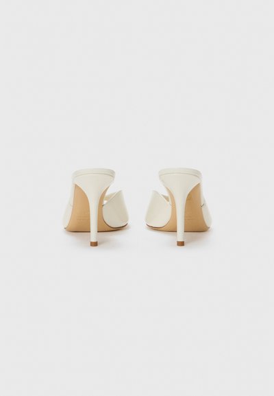 Pantofi cu toc înalt, albi, cu o textură uniformă, spate deschis și un design curbat. Toc subțire și talpă de nuanță bej deschis. Stil minimalist.