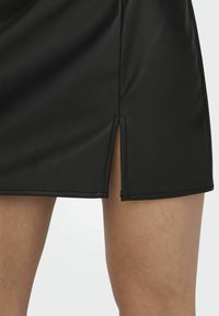 Zwarte faux leren mini-skirt met een zijscheur, een soepele textuur, strakke lijnen en zichtbare stiksels langs de zoom.