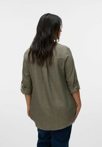 Chemise à manches longues, vert olive, à boutons. Tissu léger et texturé avec des manches roulées et une coupe légèrement décontractée, descendant au-delà de la taille.