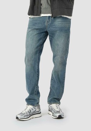 Lysblå jeans med lige ben-design, lavet af denimstof, parret med sølvfarvede sportssko med en tekstureret overdel og sorte accenter.