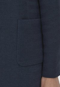 Tecido texturat navy, cu un model în țesătură de hering, cu un detaliu al buzunarului pe partea stângă. Textură netedă cu un design structurat și adaptat.