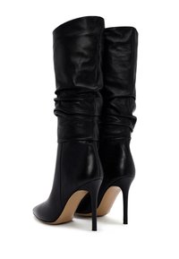 Botas de tacón stiletto de cuero negro con punta afilada, diseño hasta la rodilla y textura recogida en la parte superior. Presentan un tacón alto y delgado.
