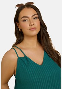 Teal, ärmlös topp med en texturerad, ribbad design och v-ringning. Har tunna axelband och ett mjukt rynk vid axlarna.