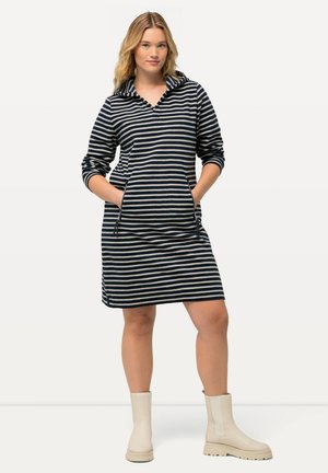Gestreiftes Kleid mit Kapuze, in Marineblau und Cremefarben, seitlichen Taschen und lässigem Schnitt. Kombiniert mit cremefarbenen Stiefeletten.