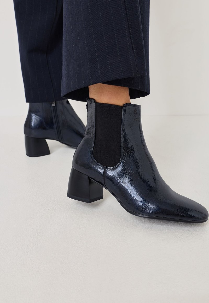 Bottines en cuir verni noir avec des panneaux latéraux élastiques, bout pointu et talon carré, associées à un pantalon à rayures bleu marine.