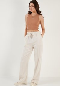 Tans ribbed crop top gecombineerd met crèmekleurige wijde sweatpants met een elastische tailleband en trekkoord; model staat met handen in de zakken.