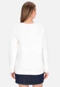 Fehér pulóver bordázott mandzsettákkal és szegéllyel, kerek nyakkivágással. Sötét farmer szoknyával párosítva, amely finom textúrát mutat.